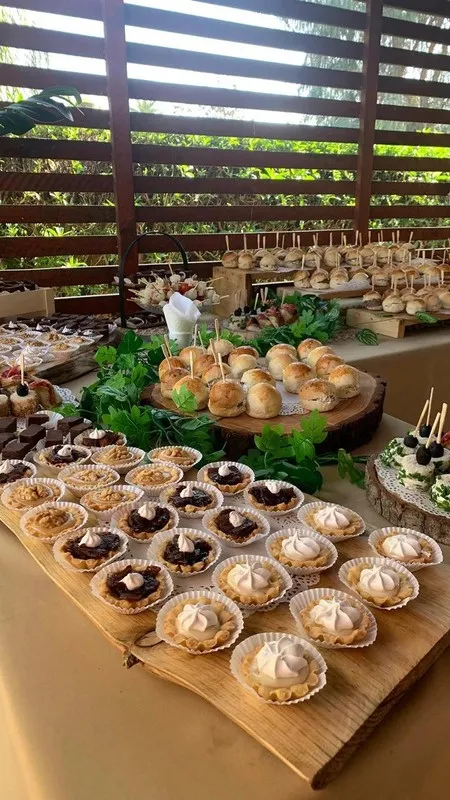 Mesa larga de dulces y bocados servida bajo una pérgola