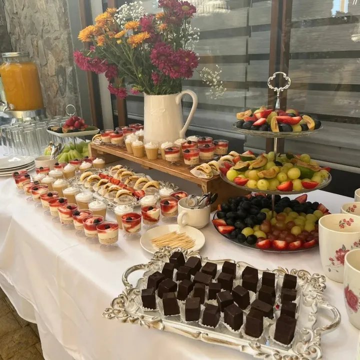 Mesa de dulces con flores frescas, frutas y vasitos de postre